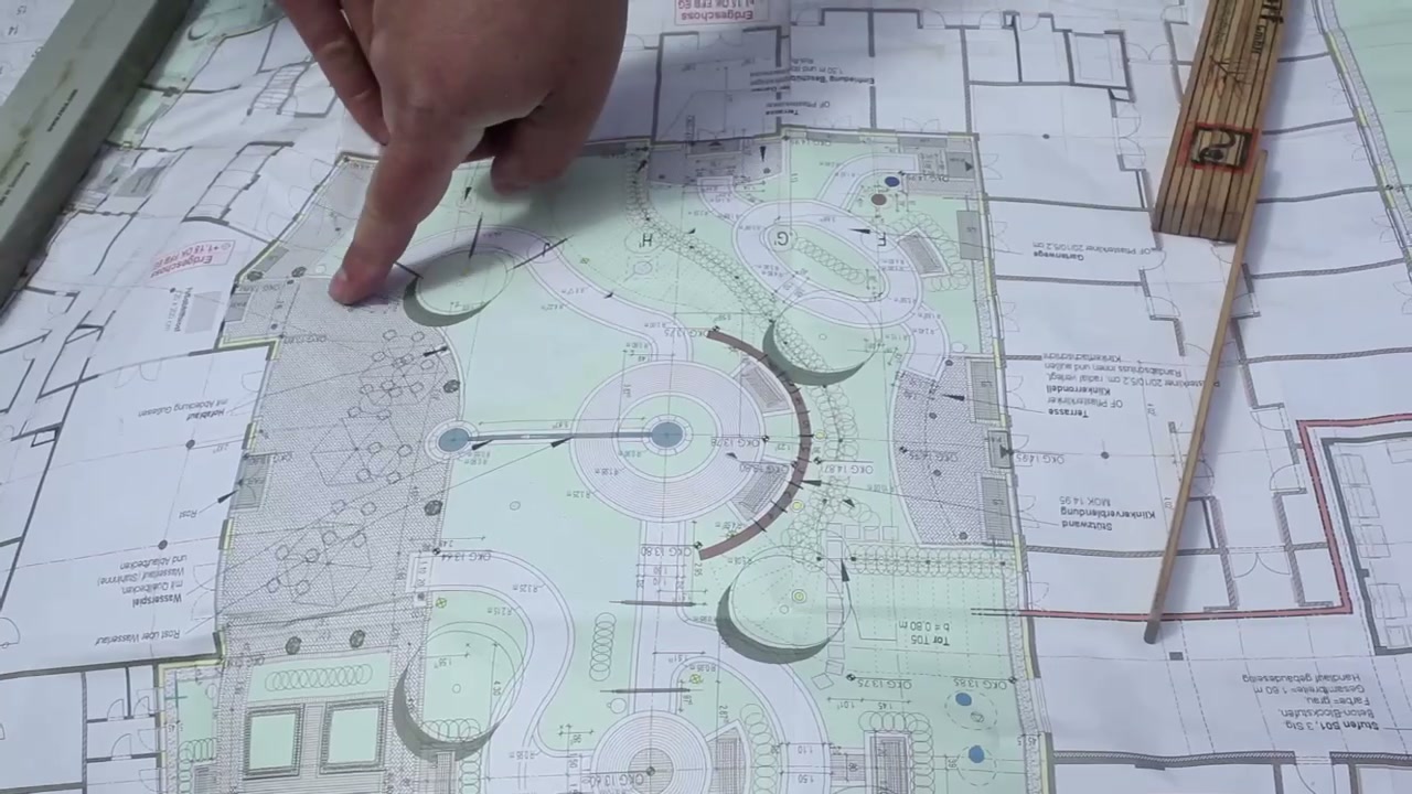 Hand bei der Planung einer Außenanlage auf einem detaillierten Lageplan